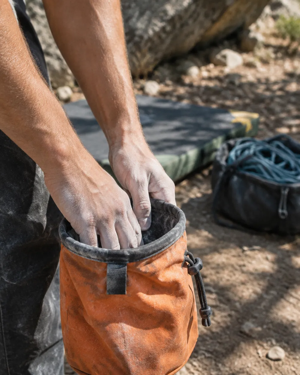 Chalky hands in an orange chalk bag at the base of a boulder